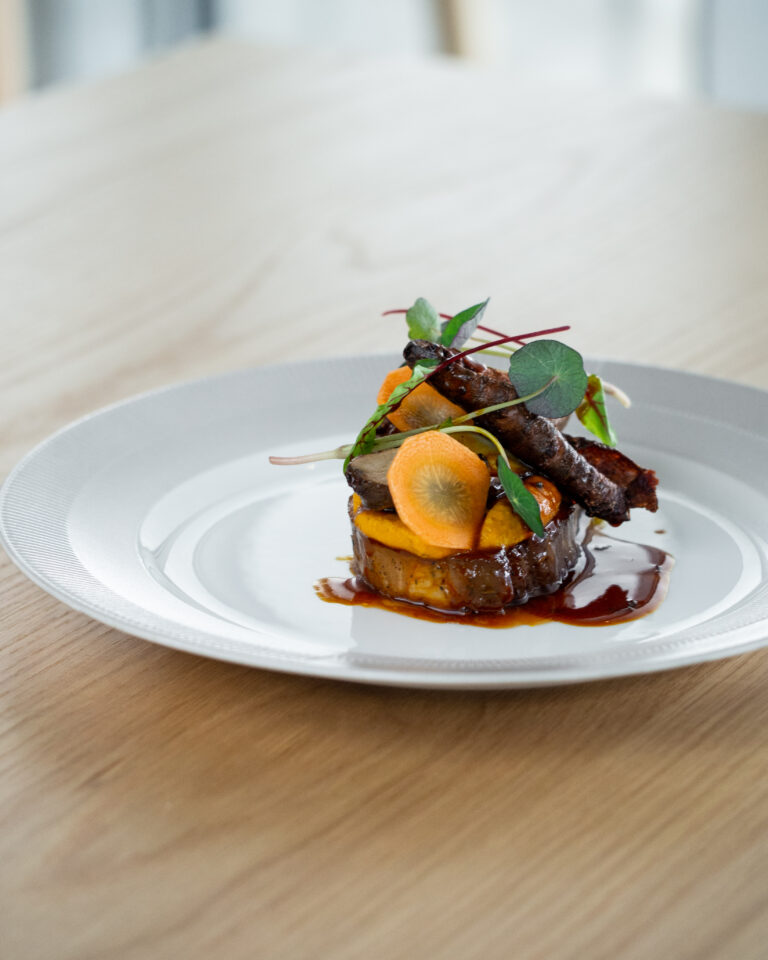 Hovedret på Restaurant GAARDEN i Hvidovre Nakke af velfærdsgris med cremet gulerodspuré, jordskokker, urter, sauce på gulerødder, soya & brunet smør.